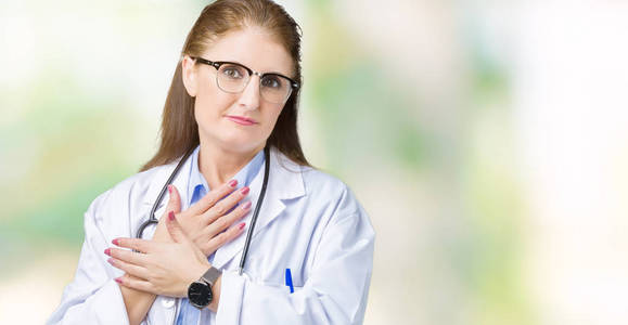 中年成熟的医生女人穿着医用外套，在孤立的背景上微笑，双手放在胸部，闭着眼睛，脸上有感激的手势。健康观念。