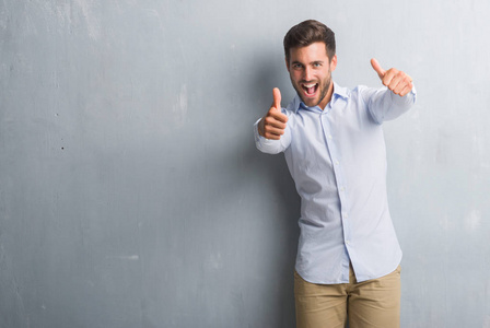 穿着灰色的灰色墙壁,用手做积极的手势,竖起大拇指,微笑着,为成功而