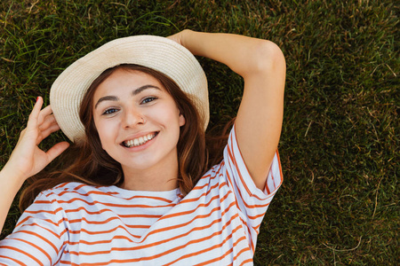 一位戴着夏帽躺在草地上脸上作鬼脸的年轻女孩的俯视图