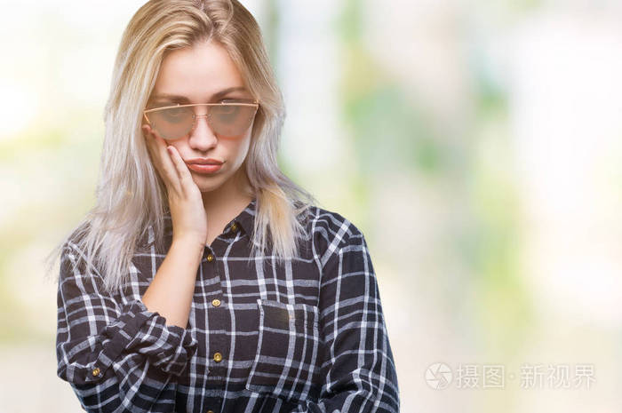 年轻的金发女人戴着太阳镜，在孤立的背景下思考，看起来疲惫，厌倦了交叉双臂的抑郁问题。