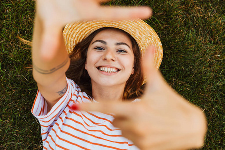 一个戴着夏帽的快乐少女，躺在草地上，双手伸着脸
