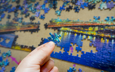 s hands collect a city puzzle on the background table. Developme