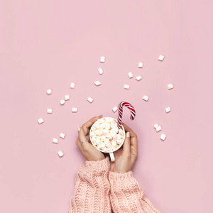 圣诞节新年饮料白色杯子与棉花糖在女性手中针织毛衣和糖果在粉红色背景顶部视图平躺冬季传统食品。 节日装饰庆祝圣诞