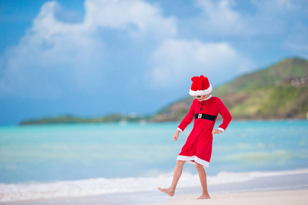 热带海滩上圣诞老人帽的可爱小女孩
