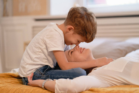 可爱的儿子和他可爱的妈妈正在抚摸他们的鼻子，一起躺在床上微笑