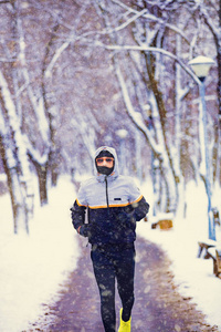 男人在下雪的公园和寒冷的天气慢跑。