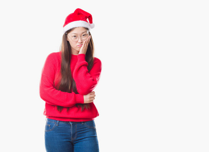 年轻的中国女人，在孤独的背景下，戴着圣诞帽，想着用交叉的手臂看起来疲倦和厌倦抑郁的问题。
