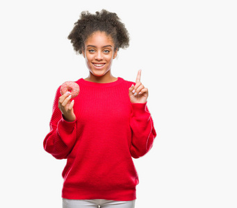年轻的美国黑人妇女吃甜甜圈，在孤立的背景下惊讶地想到了一个想法或问题，用手指指着快乐的脸第一