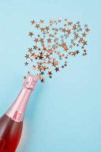 创意照片香槟瓶与纸屑在蓝色背景。 圣诞节周年庆新年庆祝概念平面图