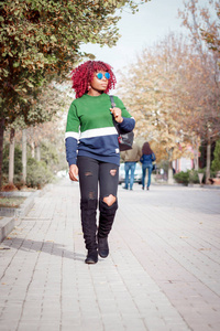 迷人的年轻非洲女性戴着蓝色太阳镜。 时尚时尚的女孩走在街上，柔和的焦点背景