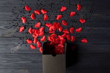 红色的心是从深蓝色的木桌上的一个黑色礼品盒里倒出来的。