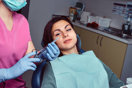 妇女患者坐在牙医椅子上, 而她的医生准备注射器注射照片