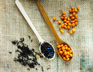 两个木制勺子与维生素健康的沙棘浆果和红茶在麻布背景。烹饪暖冬有机饮料保健食品概念