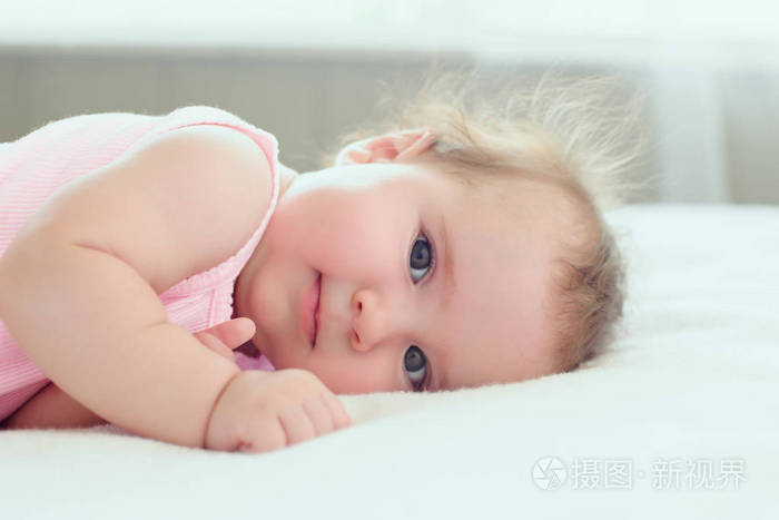 4个月大的可爱梦幻的女婴趴在床上看着镜头