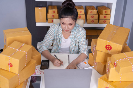 年轻女性企业家检查和写订单与纸板中小企业业务在线准备交付给客户在家办公室。