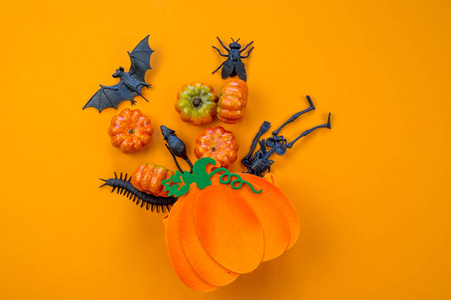 塑料南瓜和黑色玩具在橙色背景下从袋子里掉出来。 丰收节。 秋天。 很多万圣节装饰