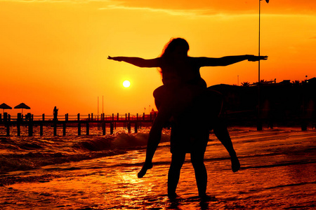日落剪影的年轻夫妇相爱拥抱在海滩。