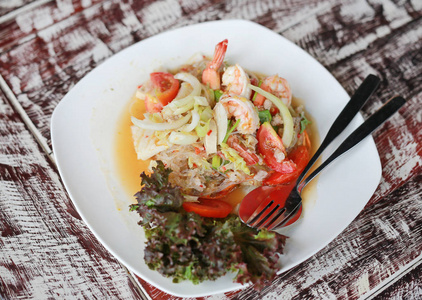 在木桌上的白色盘子里有辛辣的泰国虾沙拉。