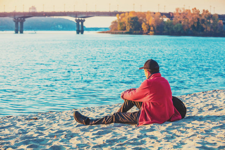 秋天，一个男人坐在河岸上看着水
