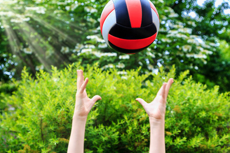 小男孩在绿树前接球打排球照片