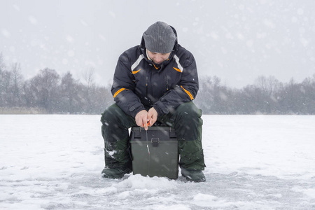 冬季捕鱼的概念。 渔夫在下雪的天气里从冰上捕鱼。