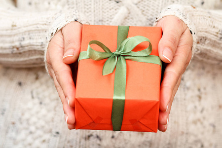 一位妇女手里拿着一个绑着绿丝带的礼盒。景深浅，选择性聚焦在盒子上。在节日或生日送礼物的概念。