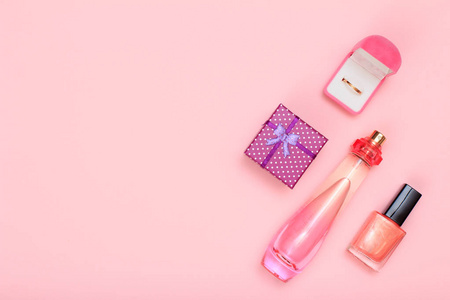 礼品盒瓶香水指甲油和金色戒指在盒子上的粉红色背景。 女性化妆品和配饰。 上面的风景。