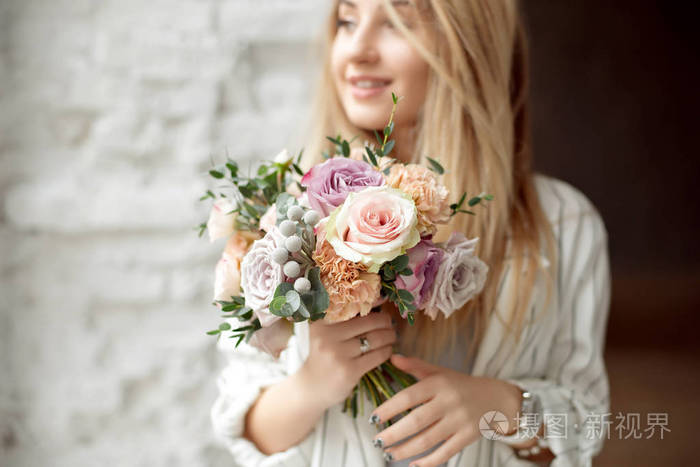 一位年轻的高加索妇女抱着一束鲜花,面带微笑地从窗户往外看,站在室内