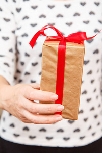女人拿着一个礼品盒，手里拿着一条红丝带。 浅场深选择性聚焦在盒子上。 节日或生日礼物的概念。