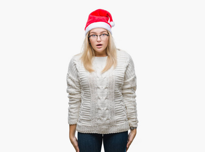 年轻的高加索女人戴着圣诞帽，在孤立的背景下害怕和震惊，惊讶的表情，恐惧和兴奋的脸。