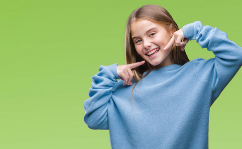 年轻漂亮的女孩穿着冬天的毛衣,在孤立的背景上微笑,自信地展示和指着