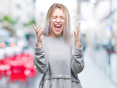 年轻的金发女人在孤立的背景下庆祝疯狂和疯狂的成功，举起手臂和闭上眼睛尖叫兴奋。 赢家概念