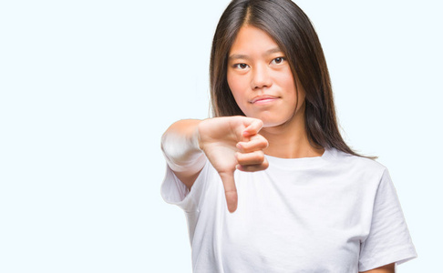 年轻的亚洲女人在孤立的背景上看起来不高兴和愤怒，表现出拒绝和消极的拇指向下的手势。 不好的表情。