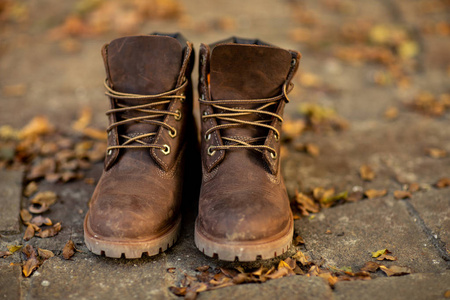 棕色皮靴站在地板上，有秋天干的叶子。 时髦的鞋子。 秋天的心情