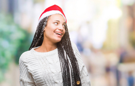 年轻的辫子非洲裔美国女孩戴着圣诞帽，在孤立的背景下，一边看着一边，脸上带着微笑，自然的表情。 自信地笑着。