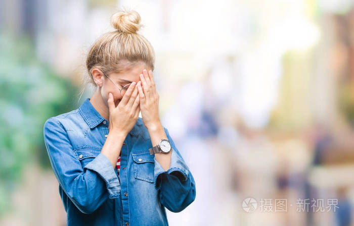 年轻漂亮的金发女人戴着眼镜在孤立的背景上悲伤的表情覆盖着脸双手