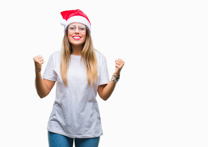 年轻漂亮的女人戴着圣诞帽，在孤立的背景上庆祝，惊讶和惊讶的成功，举起手臂和睁开眼睛。 赢家概念。