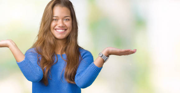 年轻漂亮的黑发女人，穿着蓝色毛衣，背景与世隔绝，微笑着双手张开手掌，展示和广告比较，平衡