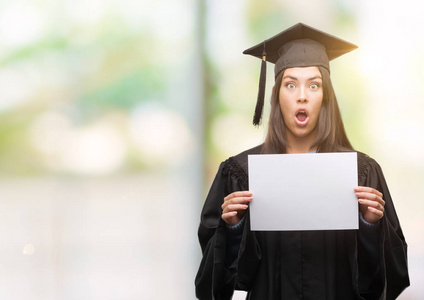 年轻的西班牙裔妇女穿着毕业制服，拿着毕业证书纸，吓得满脸惊讶，恐惧和兴奋的表情