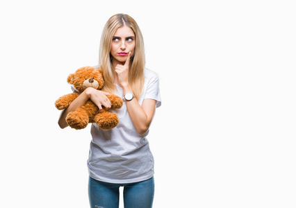 年轻漂亮的金发女人抱着玩具熊在孤立的背景下严肃的脸思考问题，很困惑的想法