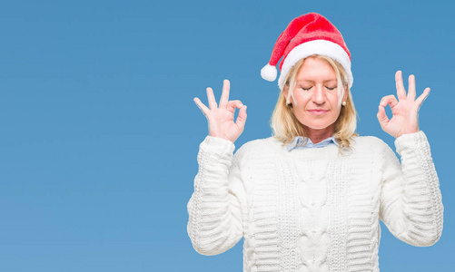 中年金发女人戴着圣诞帽，在与世隔绝的背景下放松，闭着眼睛微笑，用手指做冥想手势。瑜伽概念。