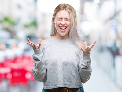 年轻的金发女人在孤立的背景下庆祝疯狂和疯狂的成功，举起手臂和闭上眼睛尖叫兴奋。 赢家概念