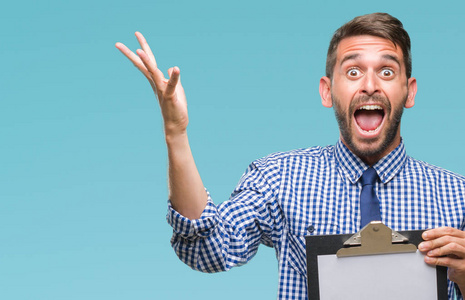 年轻英俊的商人拿着剪贴板在孤立的背景上非常高兴和兴奋,胜利者的