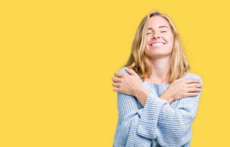 美丽的年轻女子穿着蓝色毛衣,在孤立的背景下拥抱自己,快乐而积极