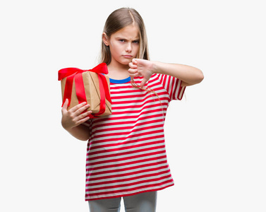 年轻漂亮的女孩，用愤怒的脸在孤立的背景上送圣诞礼物或情人节礼物，用拇指向下表示不喜欢的负面信号，拒绝的概念