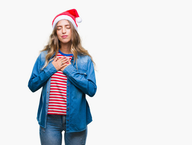 美丽的年轻金发女人戴着圣诞帽，在孤立的背景上微笑，双手放在胸前，闭着眼睛，脸上有感激的手势。健康观念。