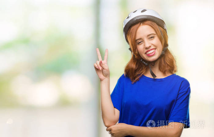 年轻漂亮的女人戴着自行车头盔，在孤立的背景上微笑，快乐的脸对着镜头眨眼，做胜利标志。第二名。