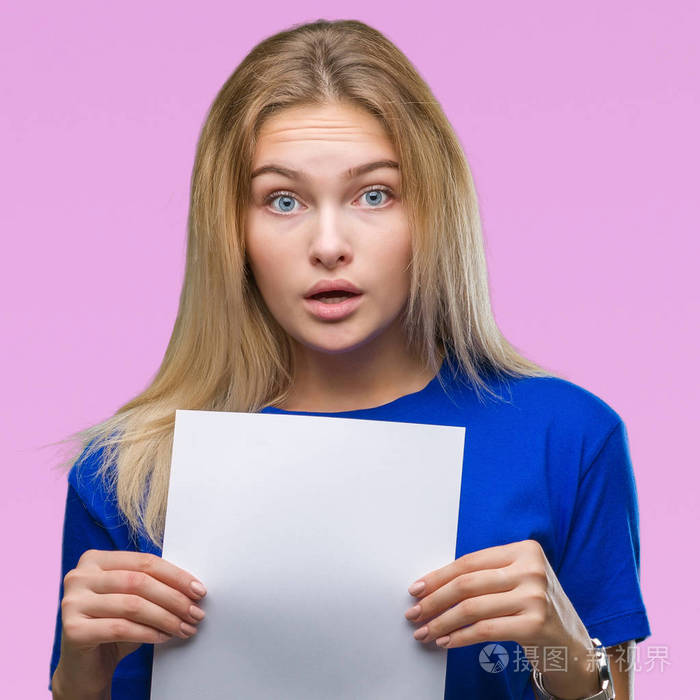 年轻的白种人女人拿着一张空白的纸在孤立的背景下吓得满脸惊讶恐惧和