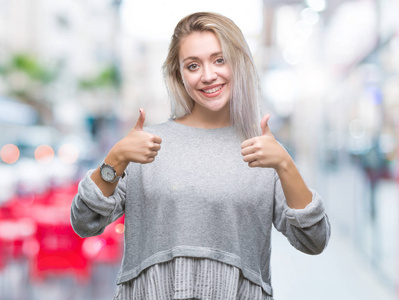 年轻的金发女人在孤立的背景成功标志做积极的手势，用手竖起大拇指，微笑和快乐。 用欢快的表情看着相机，胜利者的手势。