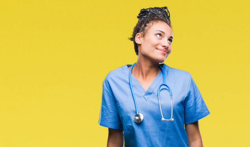 年轻的辫子非裔美国女孩专业外科医生在孤立的背景上微笑着看着一边，凝视着远方的思考。